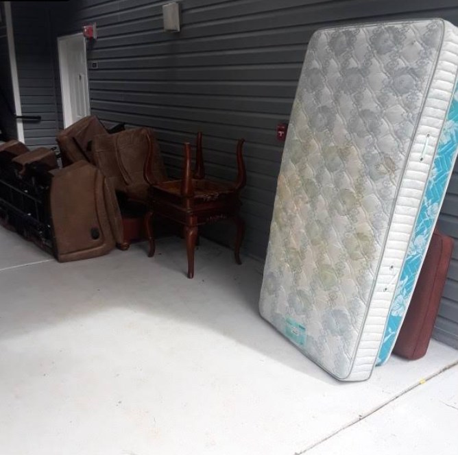 Old sofa sections, a wooden chair and a used mattress piled against a building before junk removal
